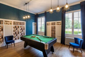 A pool table in a room with wooden flooring, bookshelves, and a view of greenery outside. - Sure Hotel by Best Western Port Jerome - Le Havre (Port-Jérôme-sur-Seine)