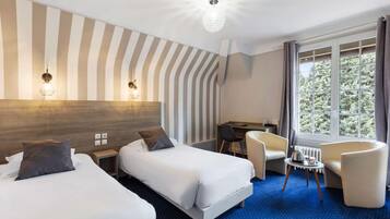 Une chambre d’hôtel avec deux lits, un bureau, une chaise et une vue sur les arbres par la fenêtre.