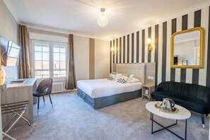 A hotel room with a bed, a desk, a chair, a black sofa, a small table with a tray, and a large mirror. - Sure Hotel by Best Western Port Jerome - Le Havre (Port-Jérôme-sur-Seine)