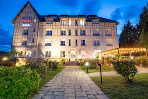 Un hôtel avec une enseigne bien visible indiquant « HÔTEL », une entrée centrale avec des marches et une façade bien éclairée.