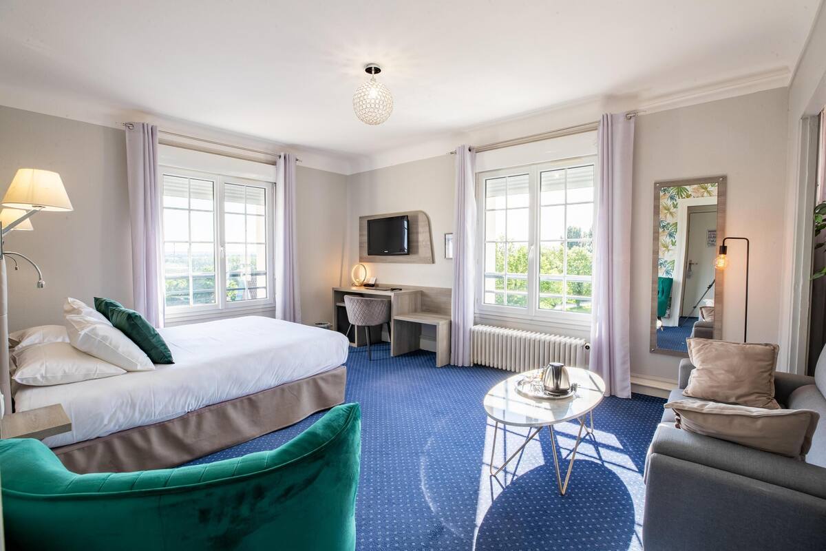 Une chambre d’hôtel avec un lit, un bureau, une chaise, une petite table et un téléviseur.