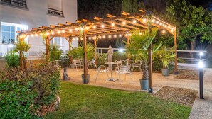 An outdoor patio with a wooden pergola, string lights, and seating. - Sure Hotel by Best Western Port Jerome - Le Havre (Port-Jérôme-sur-Seine)