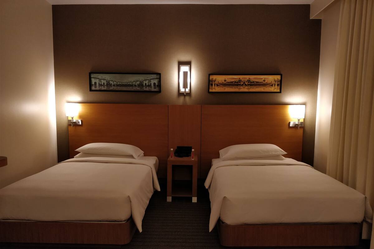 A hotel room with two beds, a nightstand, and two wall-mounted lamps.