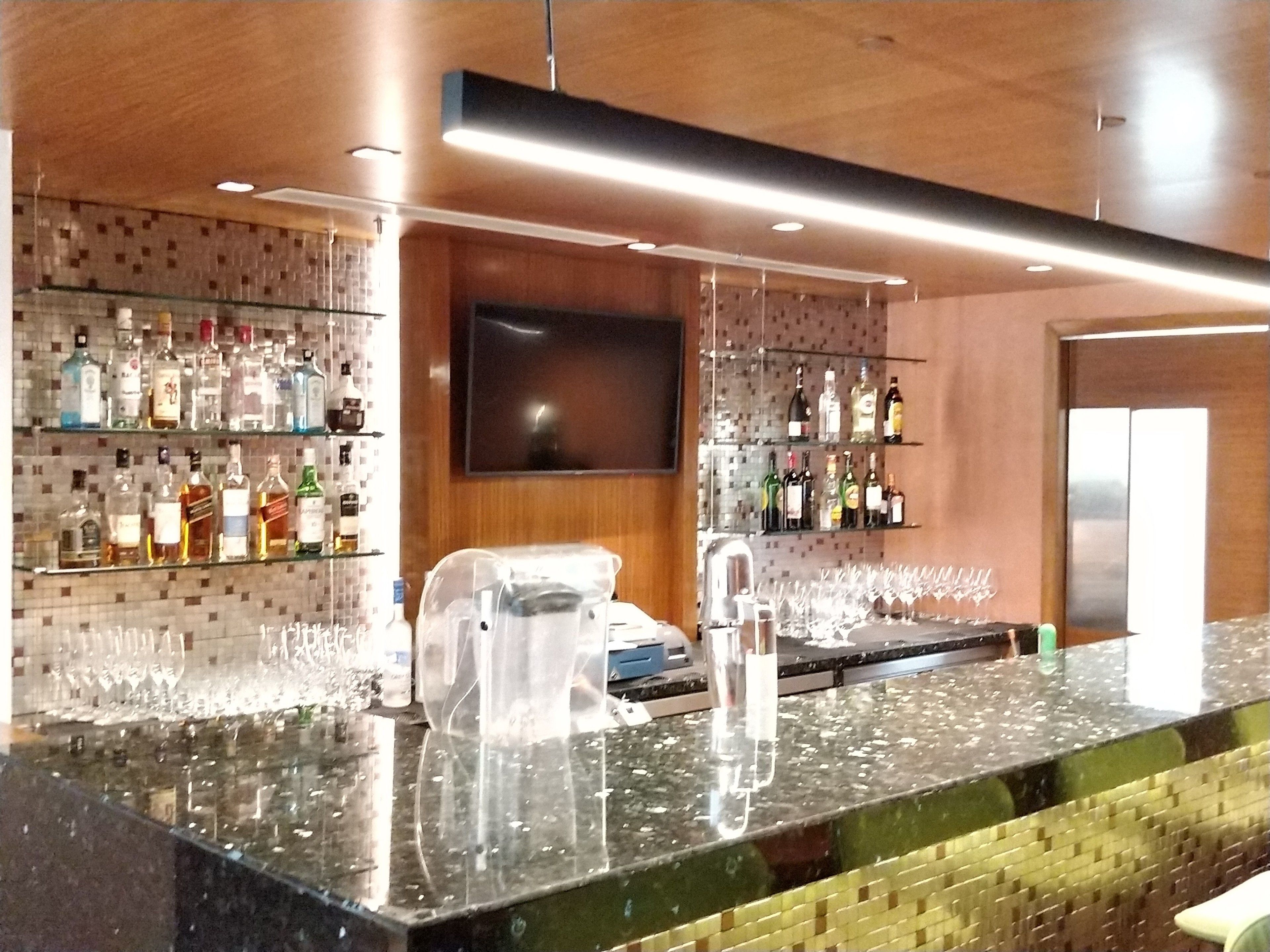 Een bar met een toonbank, flessenkasten vol drank, een televisie en een betegelde muur.