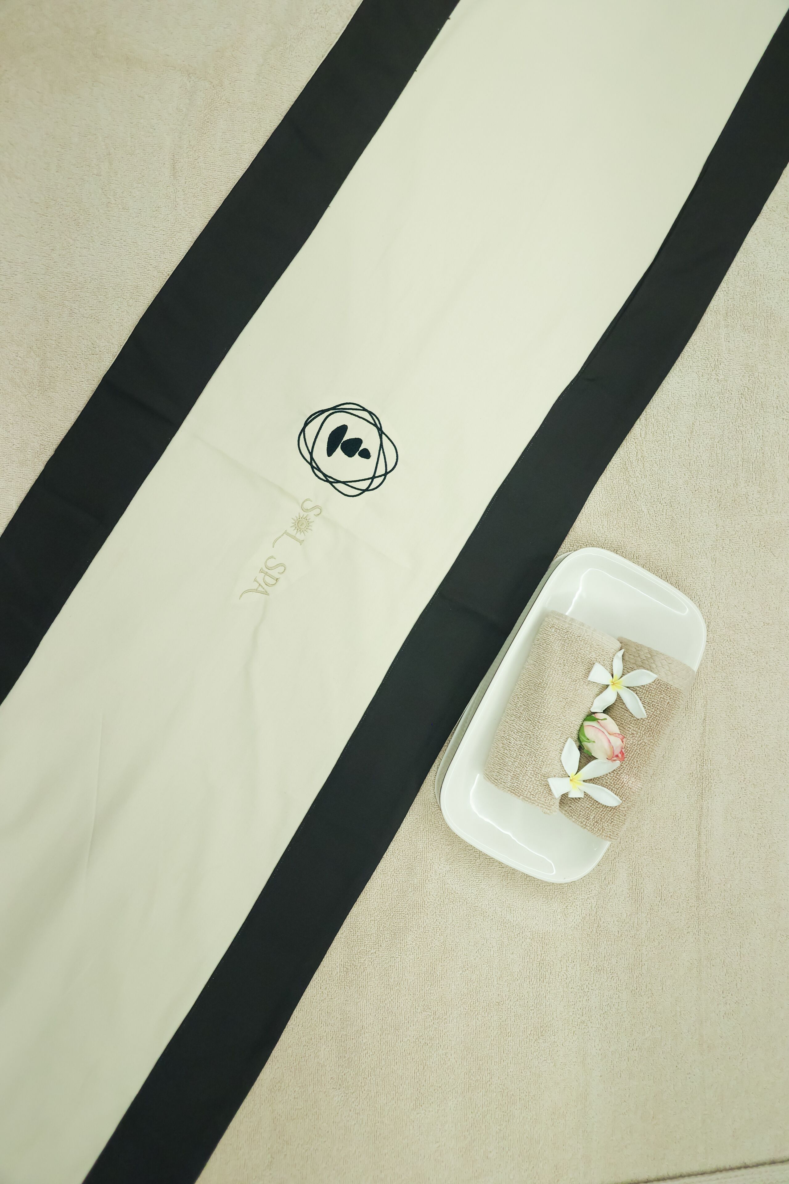 A white towel with a black stripe and a logo on a beige surface.
