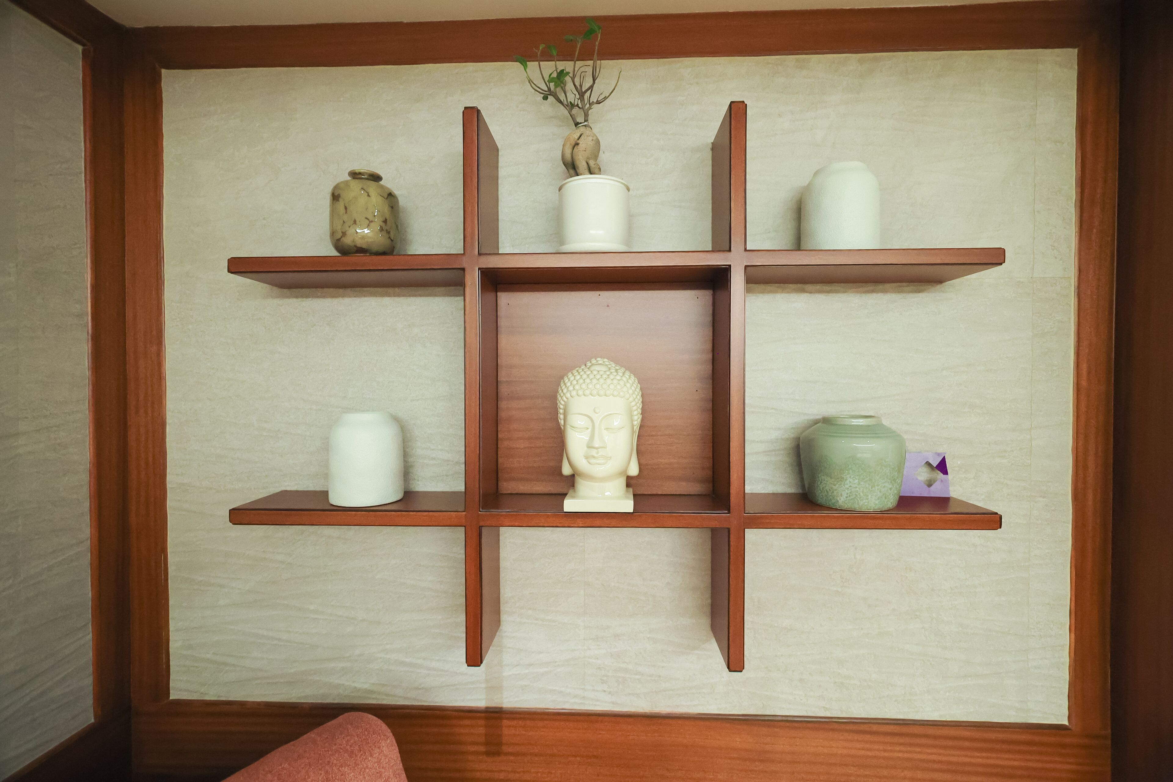 A wooden shelf unit with various decorative items including a Buddha head, vases, and a plant.
