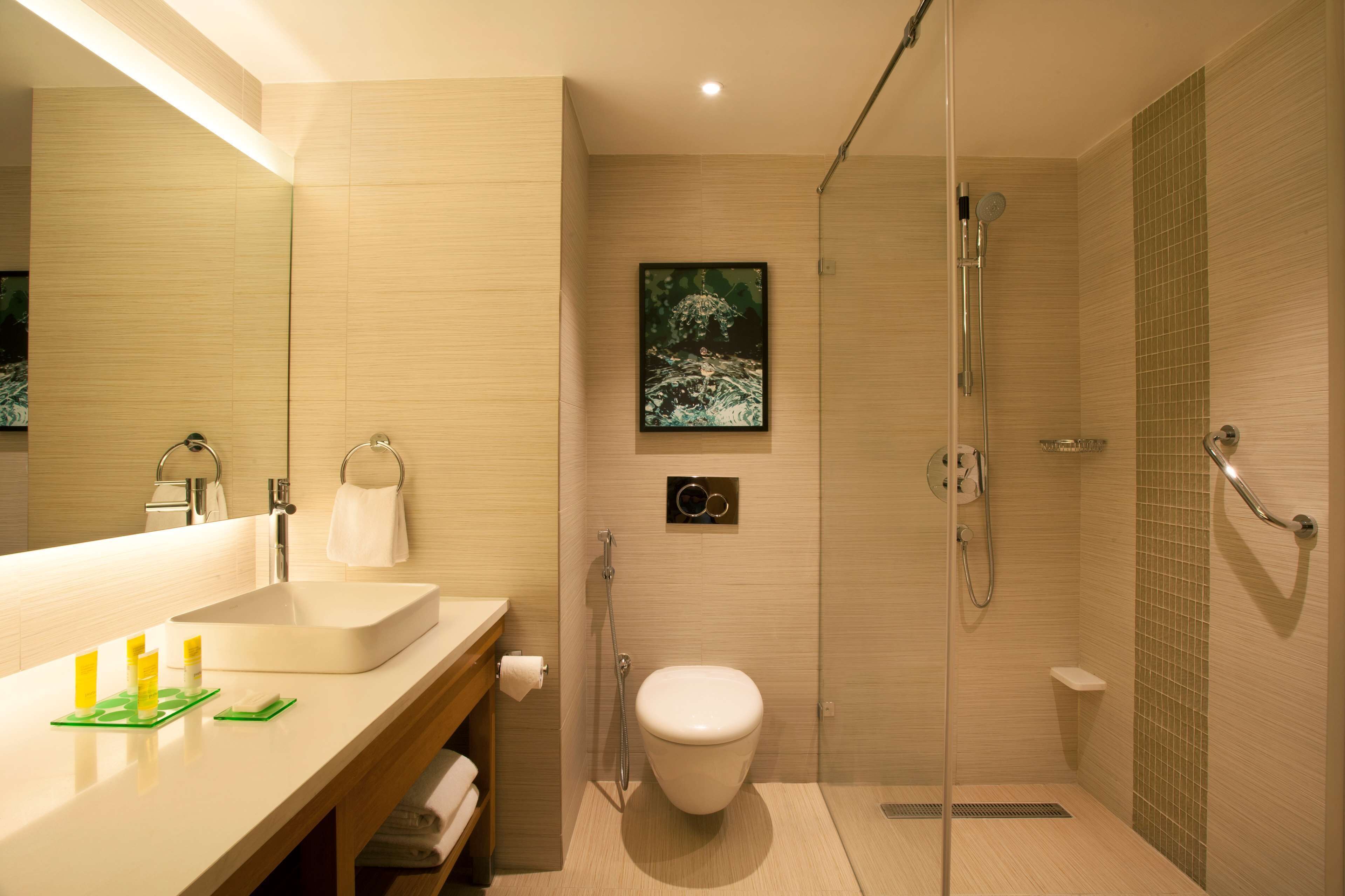 A modern bathroom with a large mirror, a sink, a toilet, and a shower area.