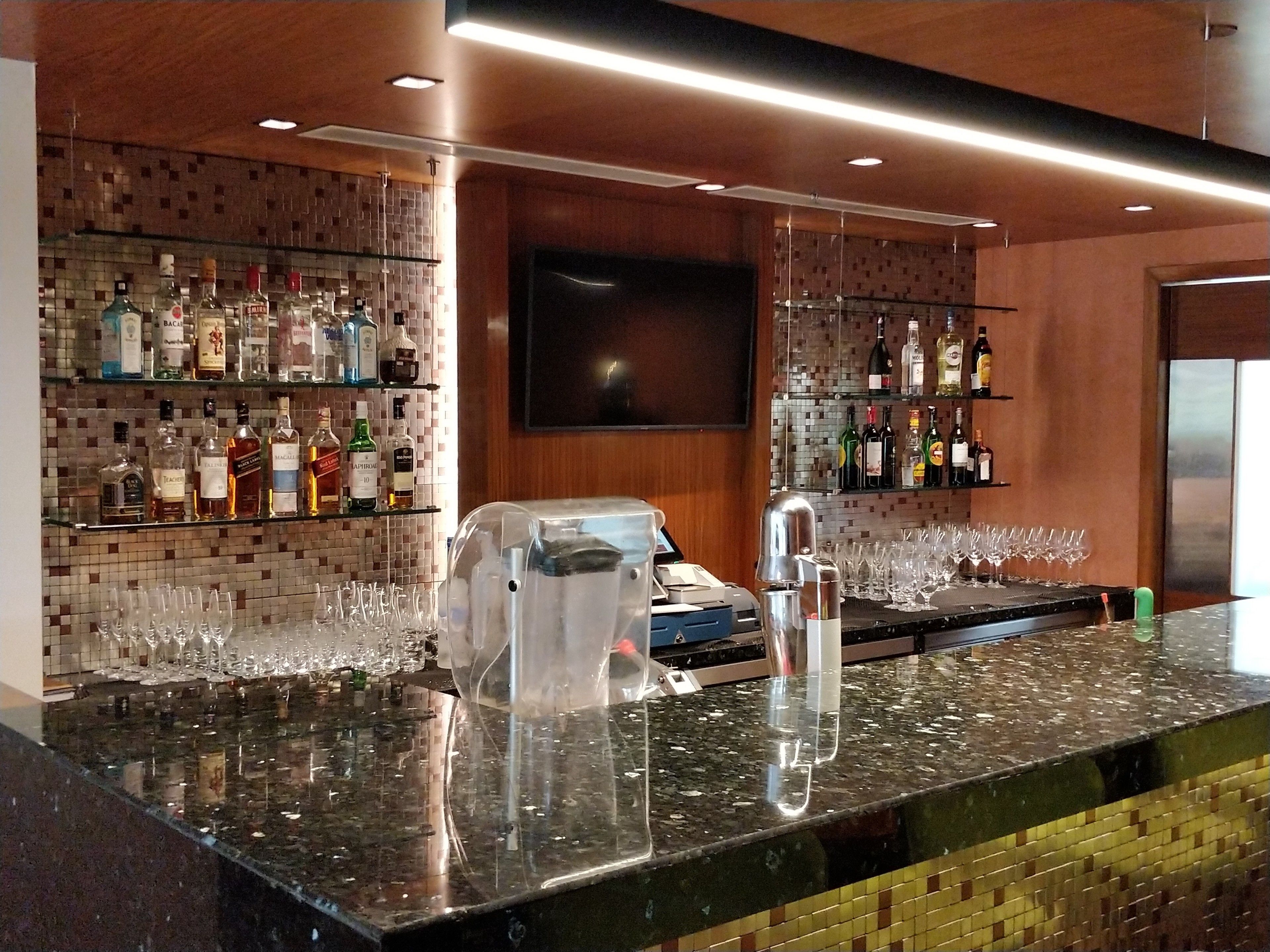 A bar area with a polished granite countertop, a cash register, and a variety of liquor bottles on shelves.