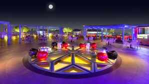 An outdoor seating area with round tables and chairs, illuminated by ambient lighting. - Hyatt Place Hyderabad Banjara Hills (Hyderabad)