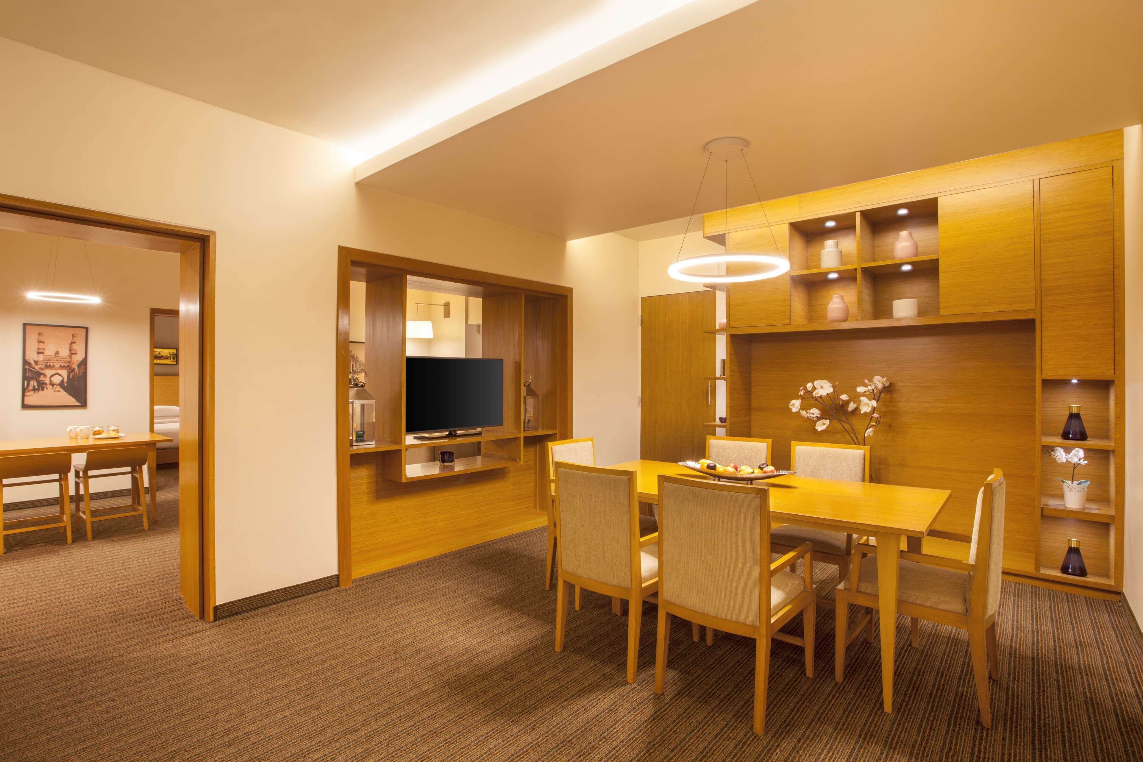 A modern dining area with a wooden table and chairs, a television, and built-in shelves with decorative items.