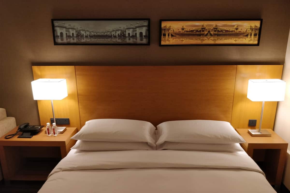 A hotel room with a large bed, two bedside tables, a wooden headboard, and two wall-mounted lamps.