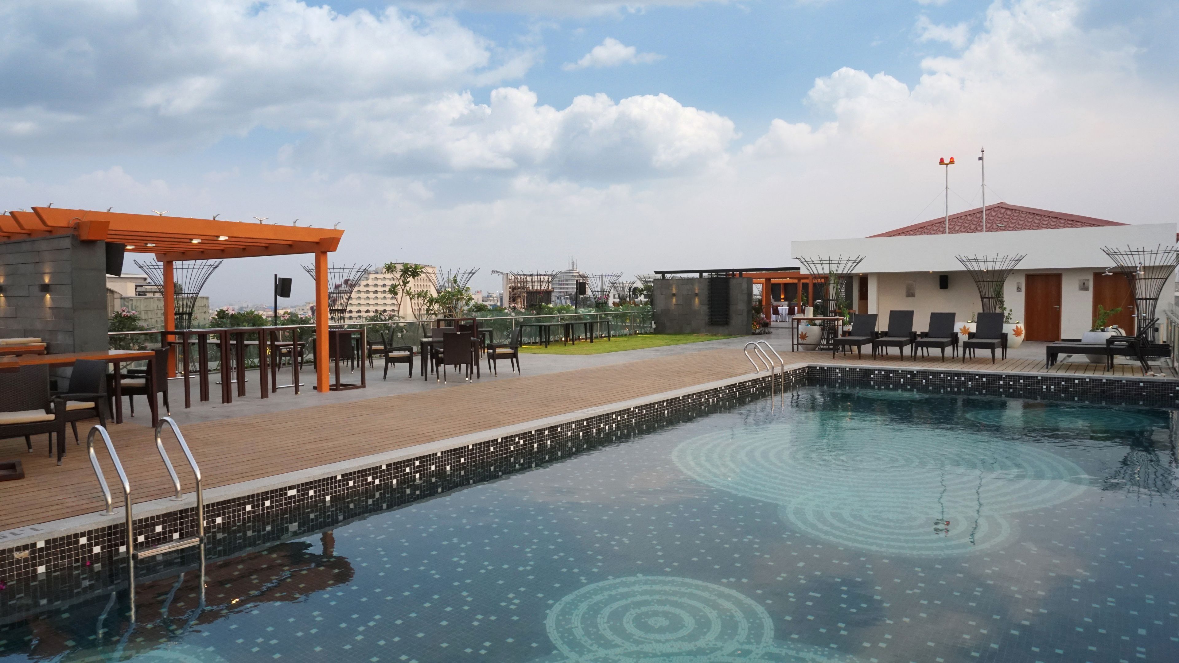 A rooftop pool area with a wooden deck, lounge chairs, and a small gazebo.