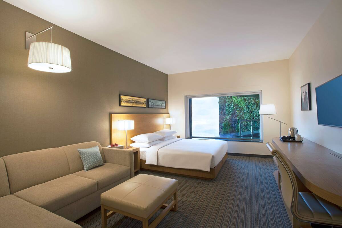 A hotel room with a bed, a sofa, a desk, and a large window.