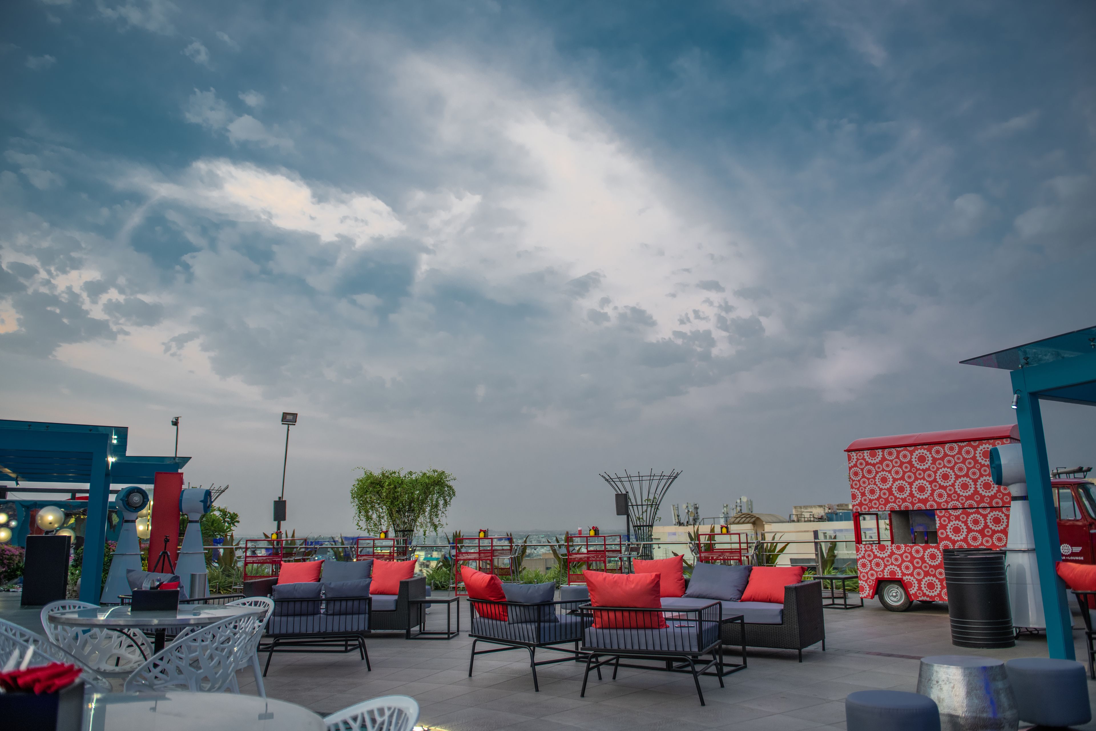 An outdoor seating area with tables and chairs, a red food truck, and a view of the city skyline.
