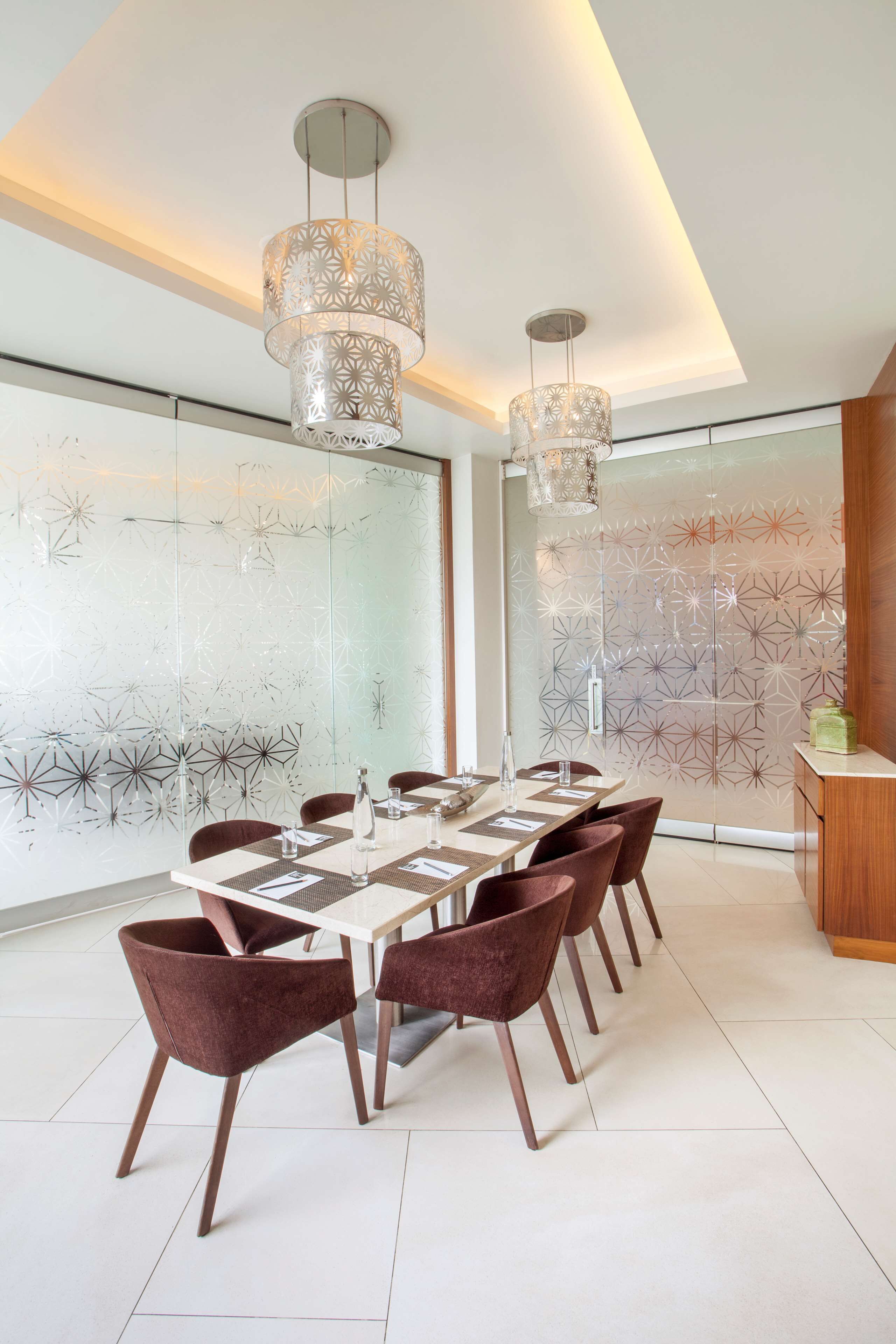Un comedor moderno con una mesa redonda, sillas marrones y lámparas decorativas colgantes.