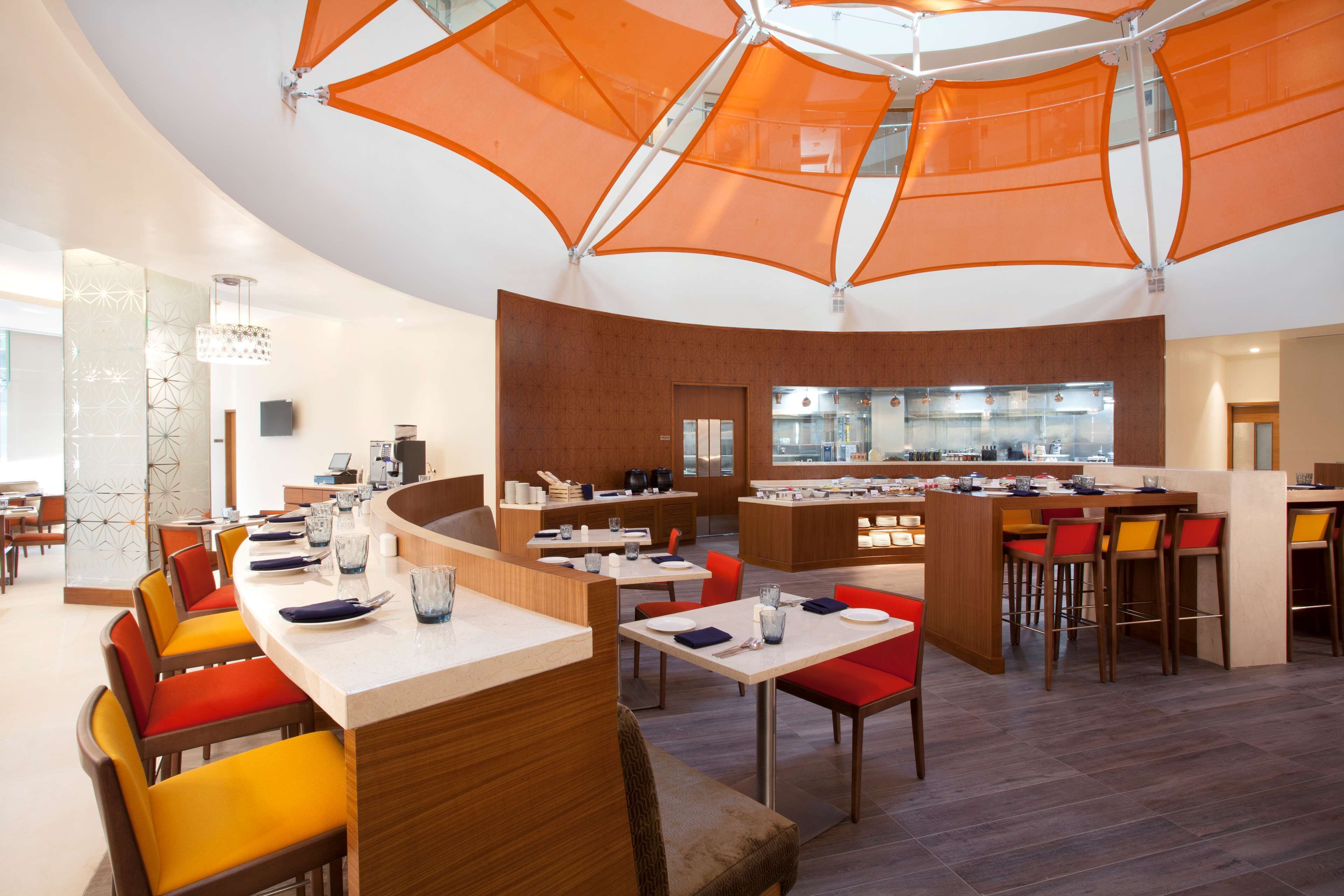 A modern restaurant with a central bar, multiple dining tables, and orange canopy overhead.