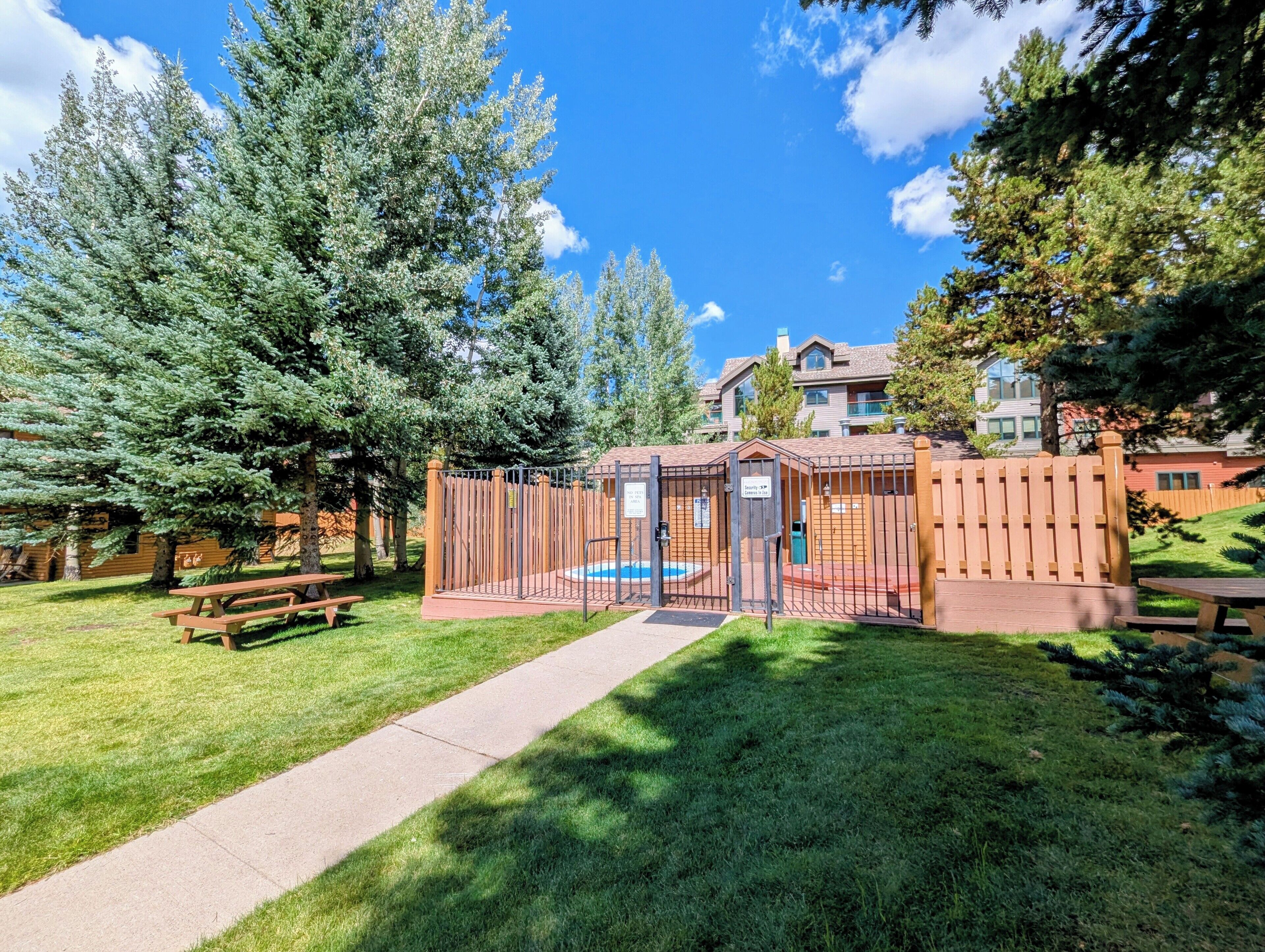 A fenced outdoor area with a pool, picnic tables, and a pathway.