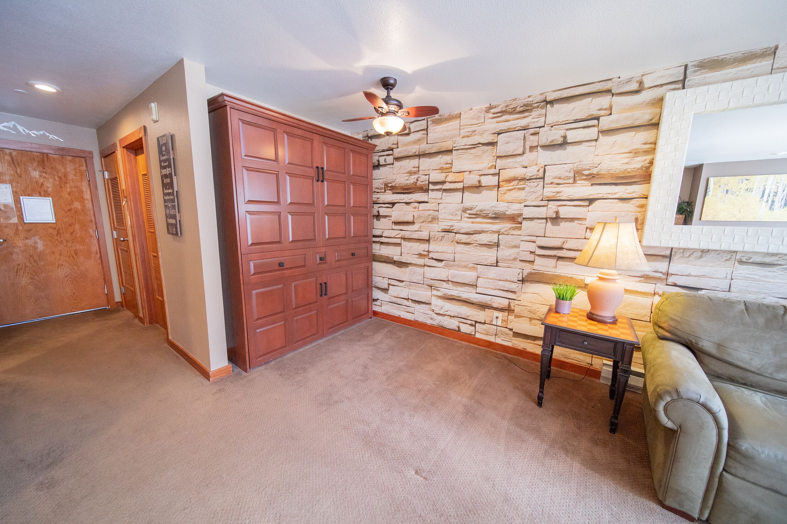 Un couloir avec un mur en pierre, une porte en bois et un ventilateur de plafond.