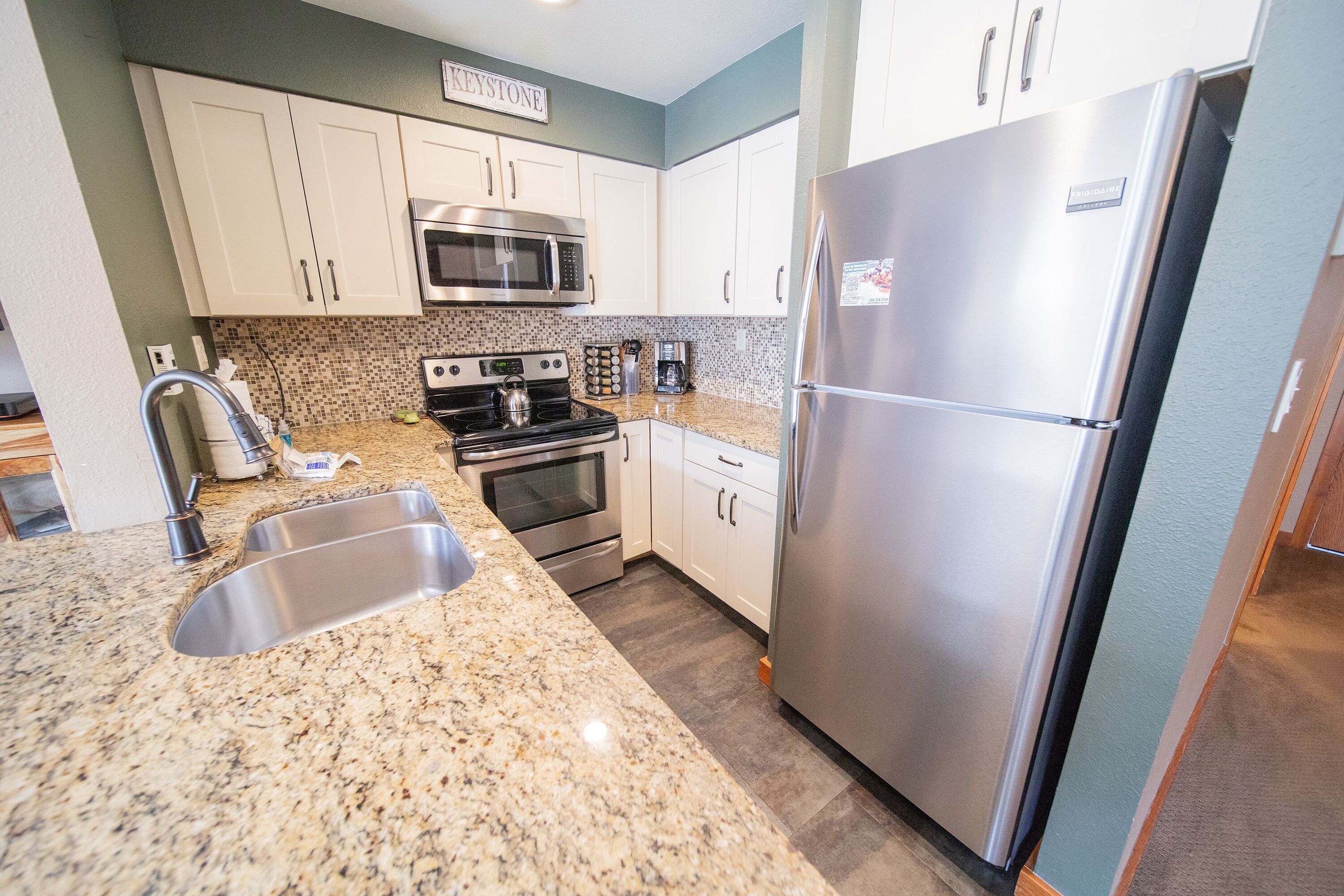 A modern kitchen with white cabinets, a stainless steel refrigerator, a microwave, and a gas stove.