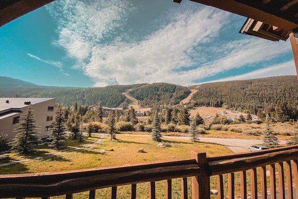 A view from a balcony overlooking a mountainous area with a ski trail, a building, and a parking area.