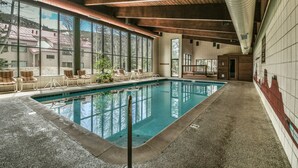 An indoor swimming pool with clear views of the outside, wooden ceiling beams, and lounge chairs along the poolside. - Ski Run 202 (Keystone)