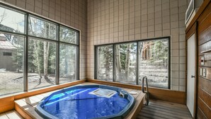 A hot tub in a room with large windows, wooden flooring, and a view of trees and a building outside. - Ski Run 202 (Keystone)