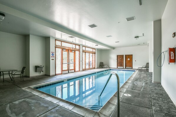 Une piscine intérieure avec des parois en verre transparent, un sol carrelé et un escalier pour accéder au bassin.