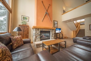 Ein Wohnzimmer mit Kamin aus Stein, Ledersofas und einem Fernseher.