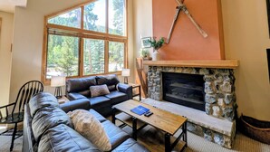 A cozy living room with a stone fireplace, a large window with a view of trees, a leather sofa, and a coffee table.