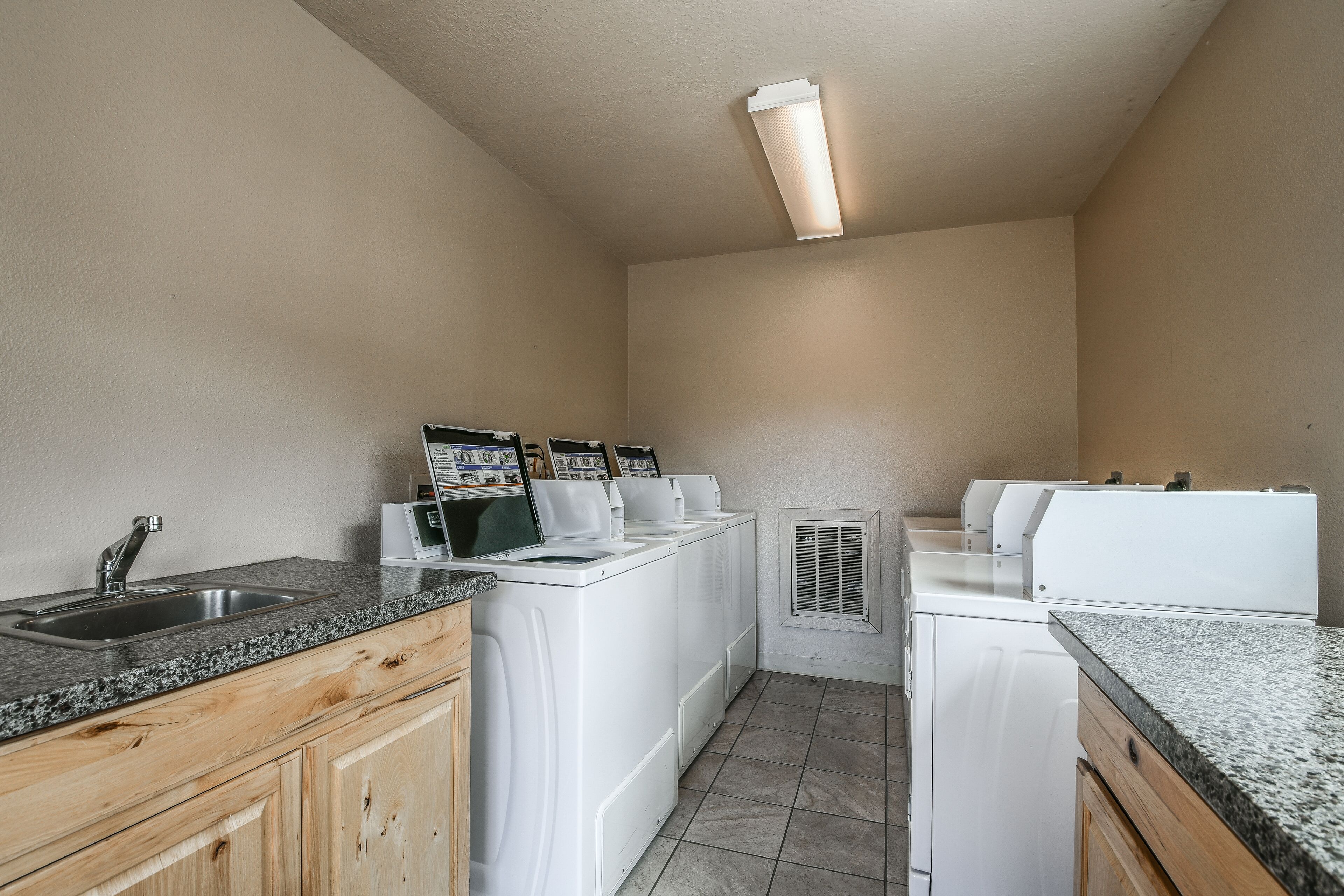 A laundry room with a sink, granite countertops, wooden cabinets, and stacked white appliances.