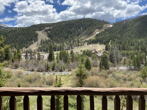 A mountain landscape with a river, a forested area, and a building with a visible driveway and parked cars.