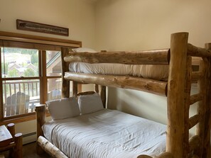 A bunk bed with white bedding, a wooden headboard, and a window with a view of a house and trees.