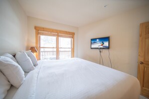 A bedroom with a large bed, a television mounted on the wall, and a wooden door.