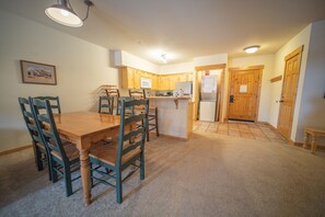 A compact kitchen with wooden cabinets, a central island, and a dining area with a wooden table and chairs. - Tenderfoot Lodge 2626 (Keystone)