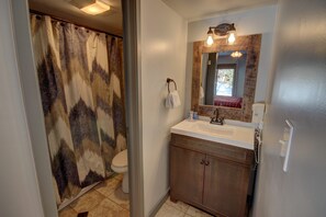 Un baño con cortina de ducha, inodoro, lavamanos, espejo y armarios de madera.