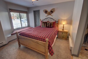 Un dormitorio con cama de madera, ventana con vistas, una puerta y una lámpara fijada a la pared.
