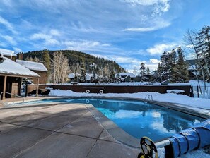 Una piscina bajo un cielo azul claro con paisajes nevados a su alrededor.