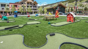 Un parcours de mini-golf avec une grange rouge, des tables de pique-nique et un espace de jeux pour enfants.