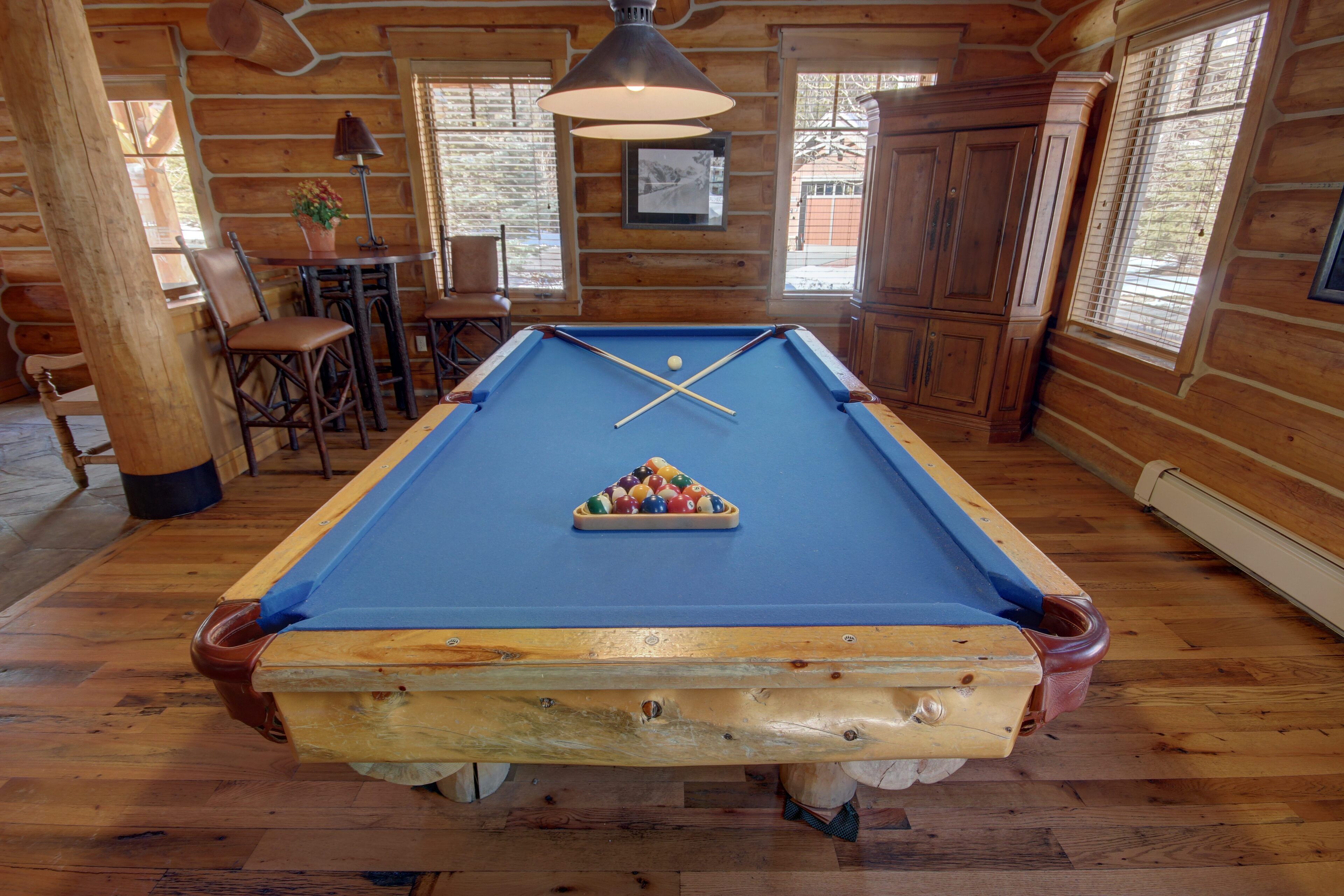 A pool table in a wooden cabin with a blue felt surface, wooden walls, and a hanging lamp.