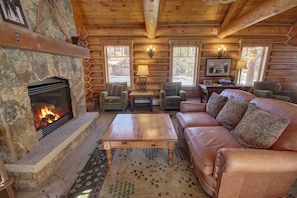 A log cabin interior with a stone fireplace, leather sofa, and wooden furniture. - Settlers Creek 6535 (Keystone)