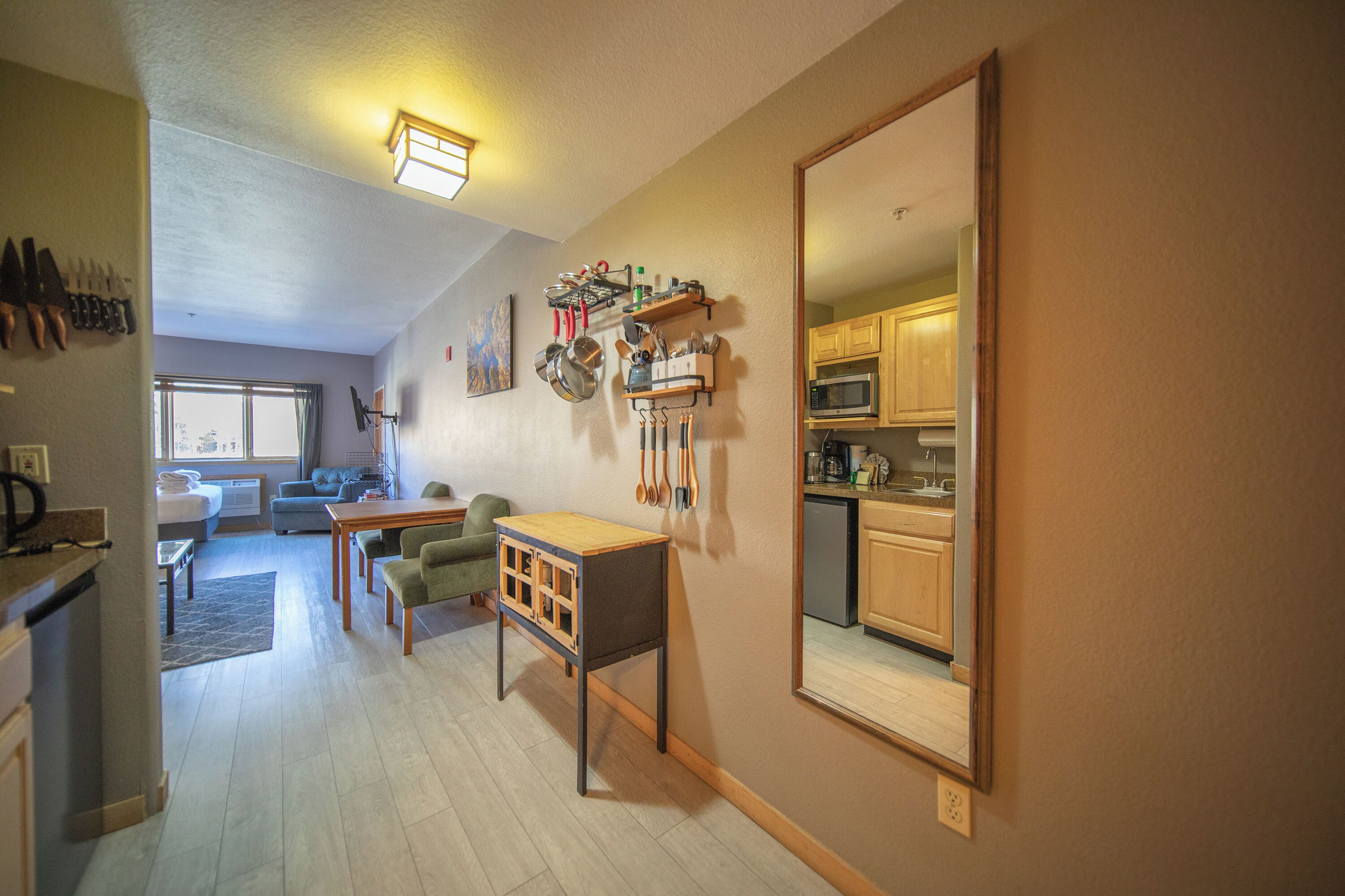 A compact living space with a kitchenette, a dining area, and a mirrored wall reflecting the kitchen.