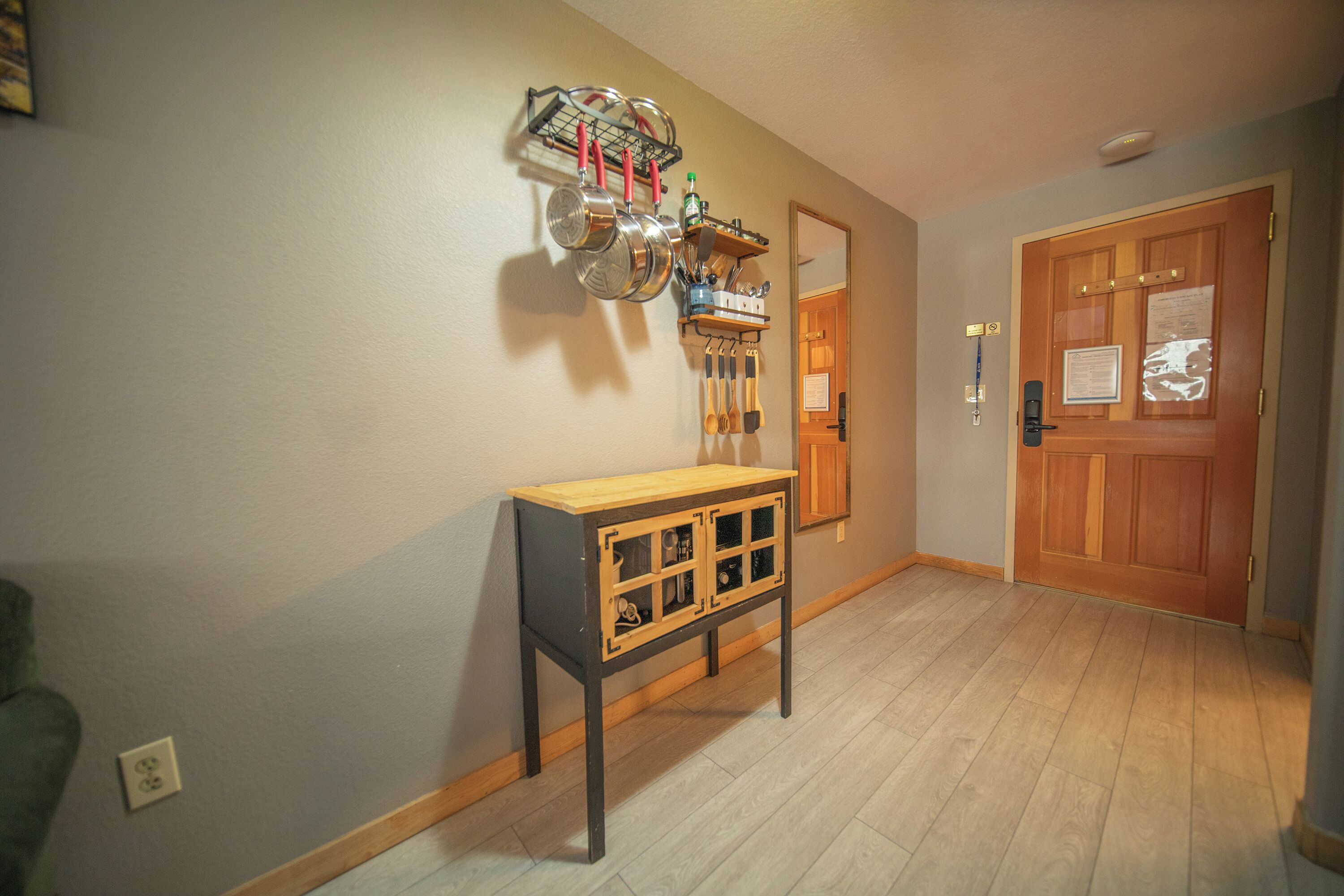 A hallway with a wooden door, a wall-mounted pot rack, and a small wooden console table.