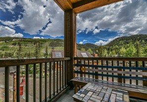 A balcony with a wooden railing overlooking a mountainous landscape with trees and a clear sky.