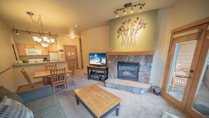 A cozy living room with a fireplace, a dining area, and a kitchen. - Arapahoe Lodge 8119 by SummitCove Lodging (Keystone)