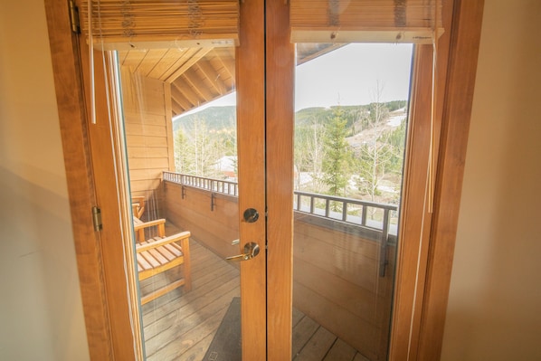 A wooden door leading to a balcony with a view of a mountainous landscape.