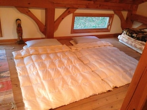 A bedroom with a large bed, wooden beams, a window, and a wooden floor. - Mcmill House (Shimoda)