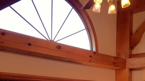 Ein Zimmer mit großem Fenster und Blick auf eine gebirgige Landschaft, Holzbalkendecke und einer gepolsterten Sitzecke mit floralem Kissen.