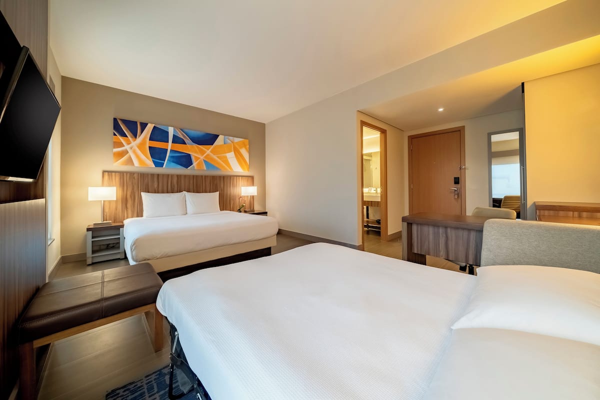 A hotel room with two beds, a TV, a desk, and a large abstract painting on the wall.