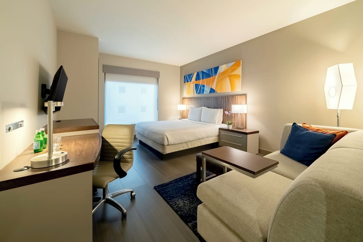 A hotel room with a bed, a desk, a chair, a sofa, and a TV.
