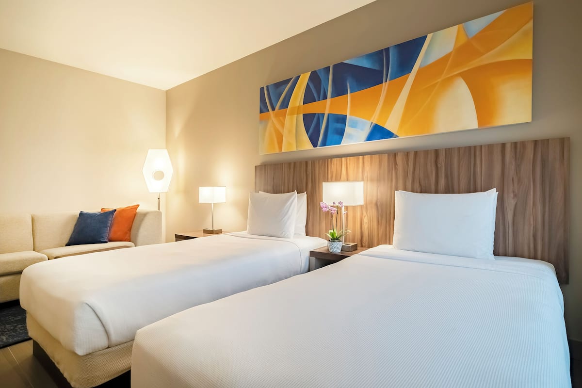 A hotel room with two beds, a sofa, and a large abstract painting on the wall.